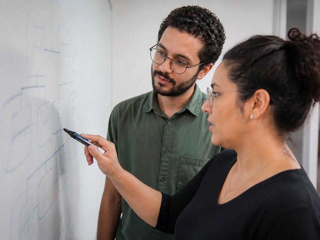 Dois alunos em pé diante do quadro branco, desenhando a ordem de um argumento